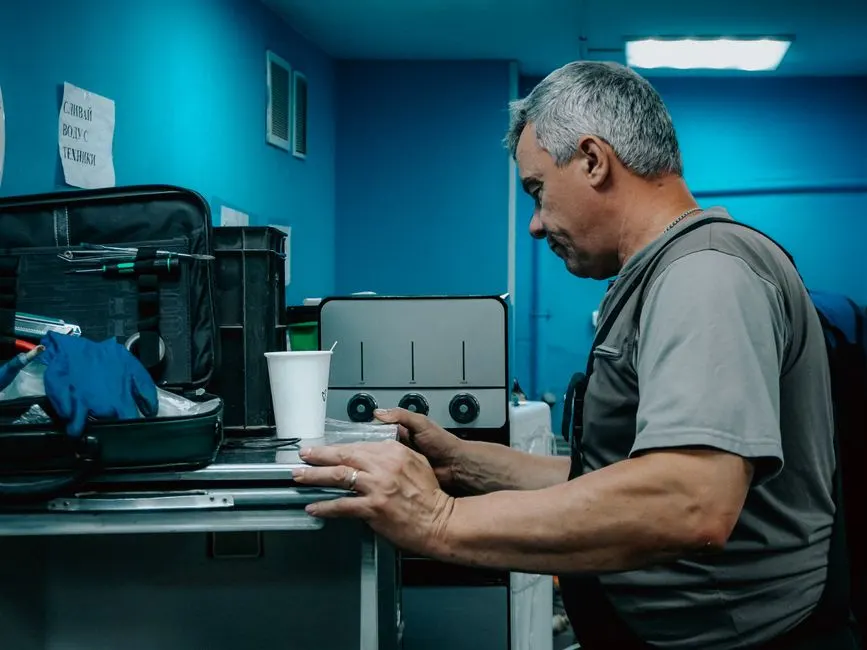 A male technician works on a machine in an industrial environment, focused on adjusting controls.